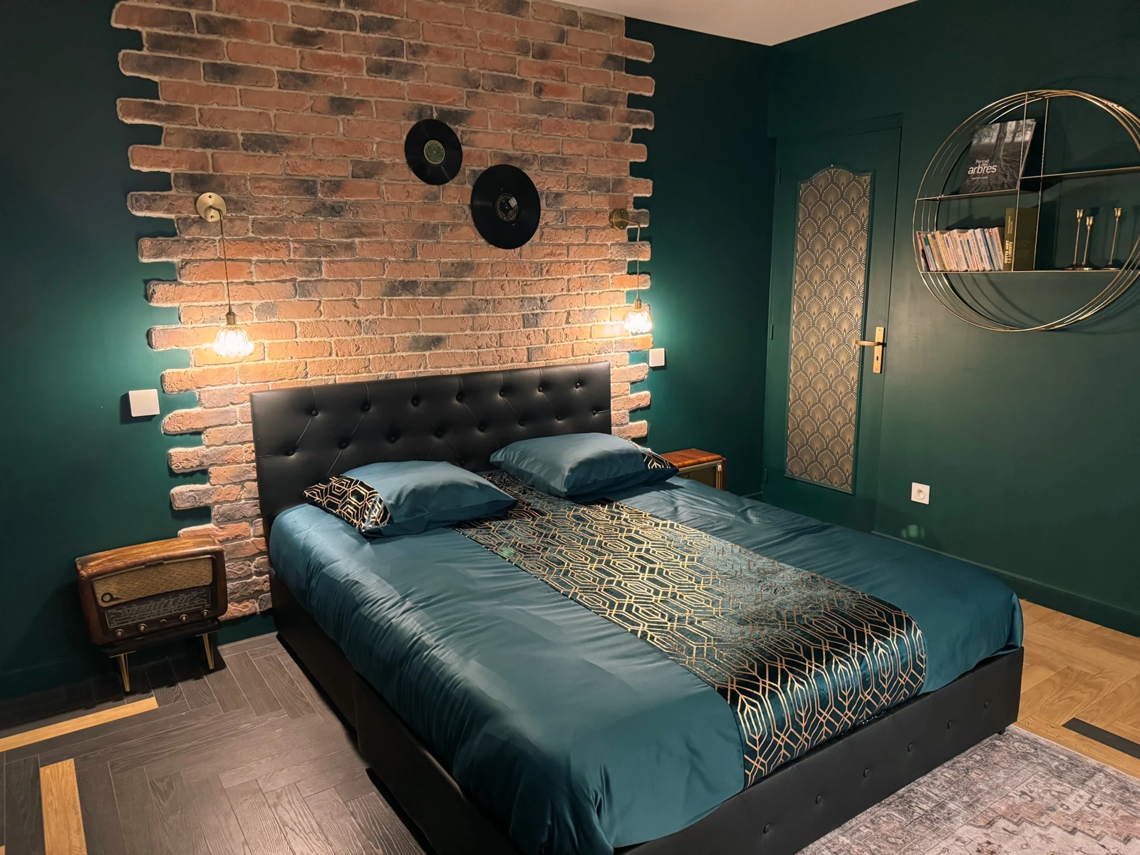 Chambre verte vintage du logement avec mur de briques, lit double et vinyles.